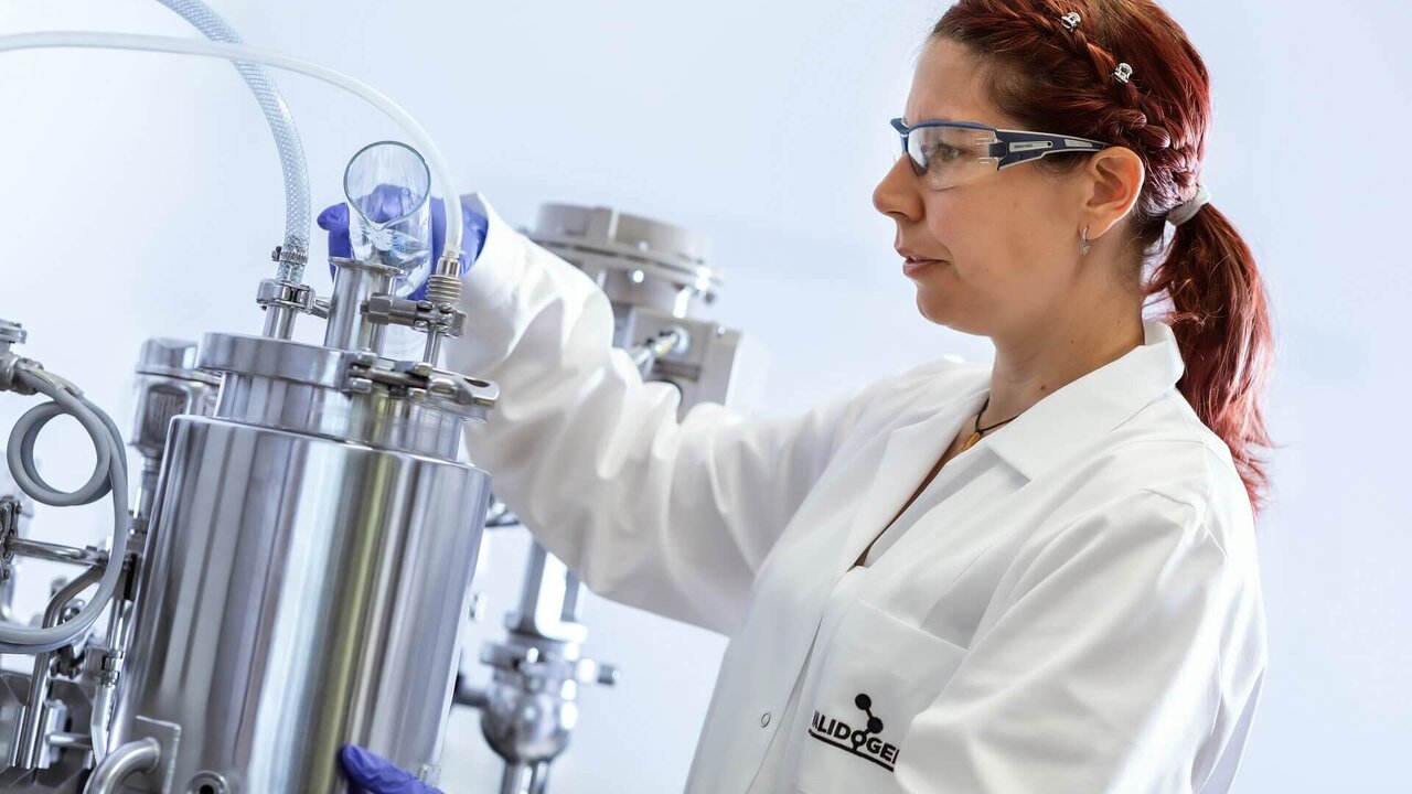 Scientist in a VALIDOGEN lab coat operating a stainless steel downstream unit.