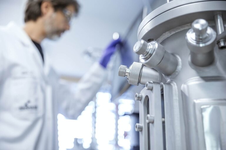 Close-up of a stainless steel bioreactor used in VALIDOGEN's fermentation process development laboratorys, with a scientist working in the background. 